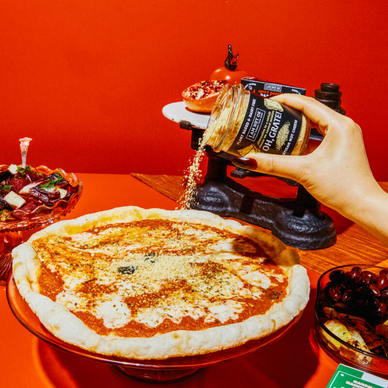 vegan parmesan sprinkled on pizza on red background