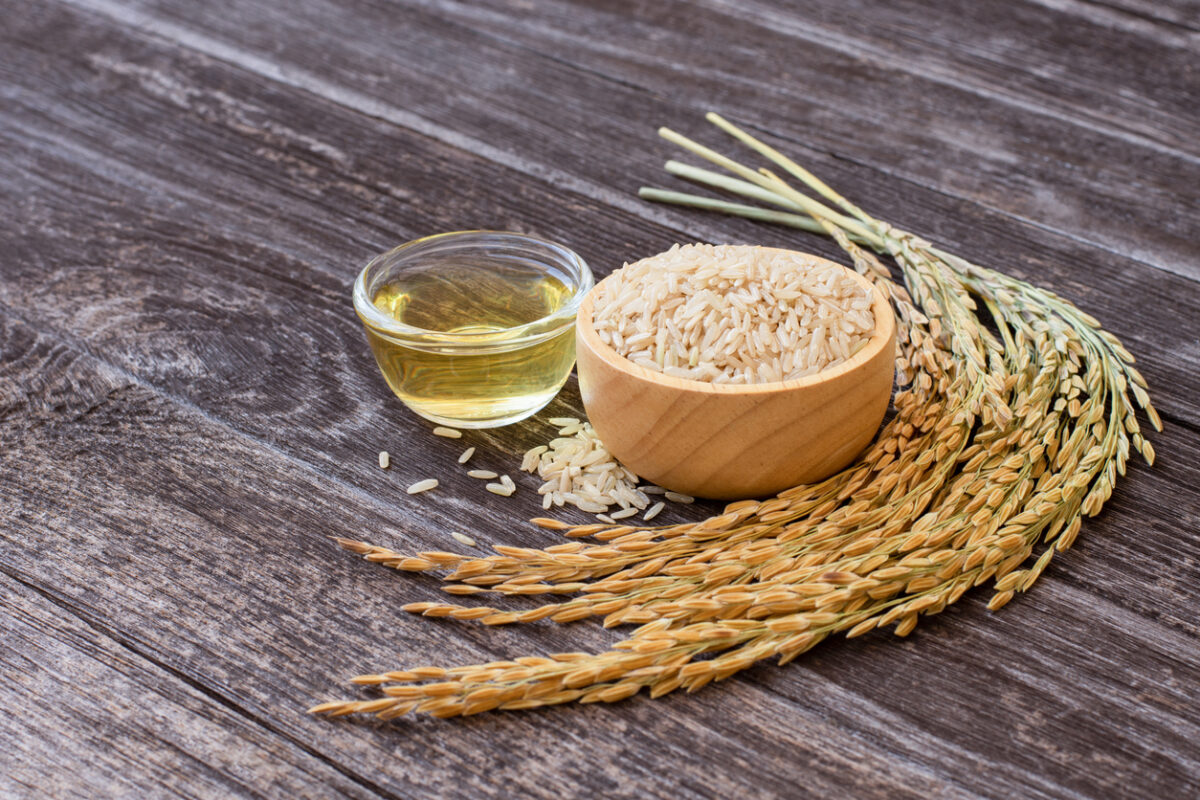 rice bran oil on wooden table with bowl of rice and wheat crop