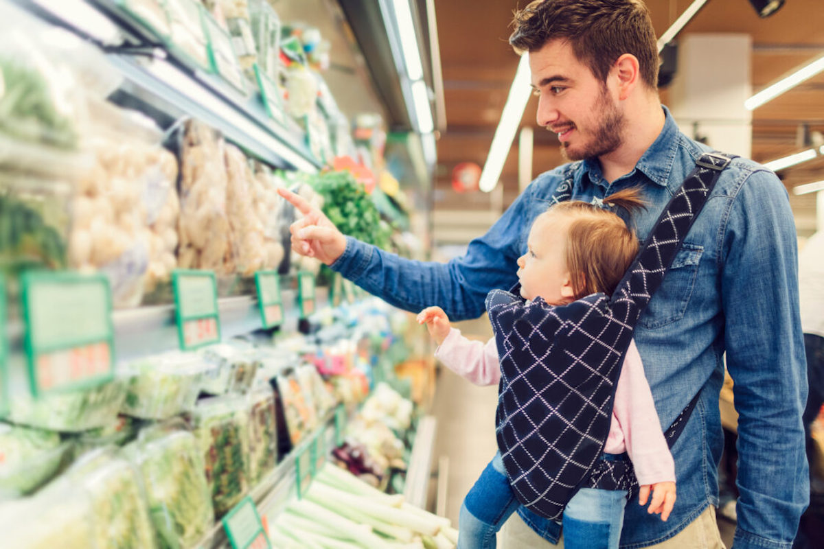 Father and baby daughter in baby carrier looking at supermarket fridge