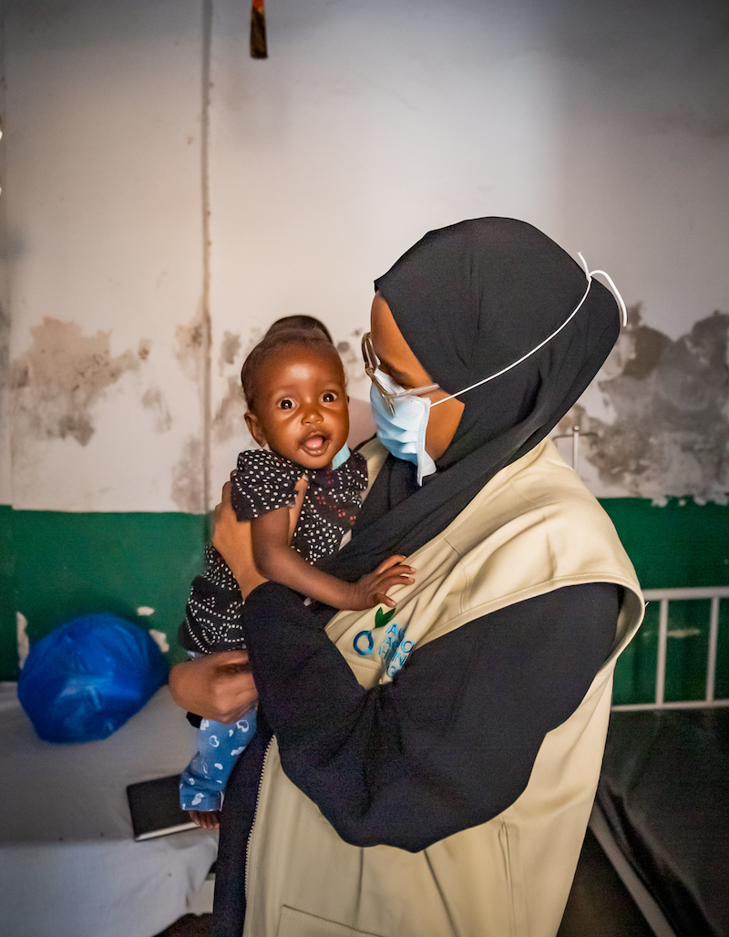Medical professional holds child in African healthcare centre