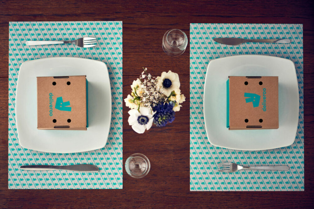 table laid with plates and cutlery containing deliveroo boxes