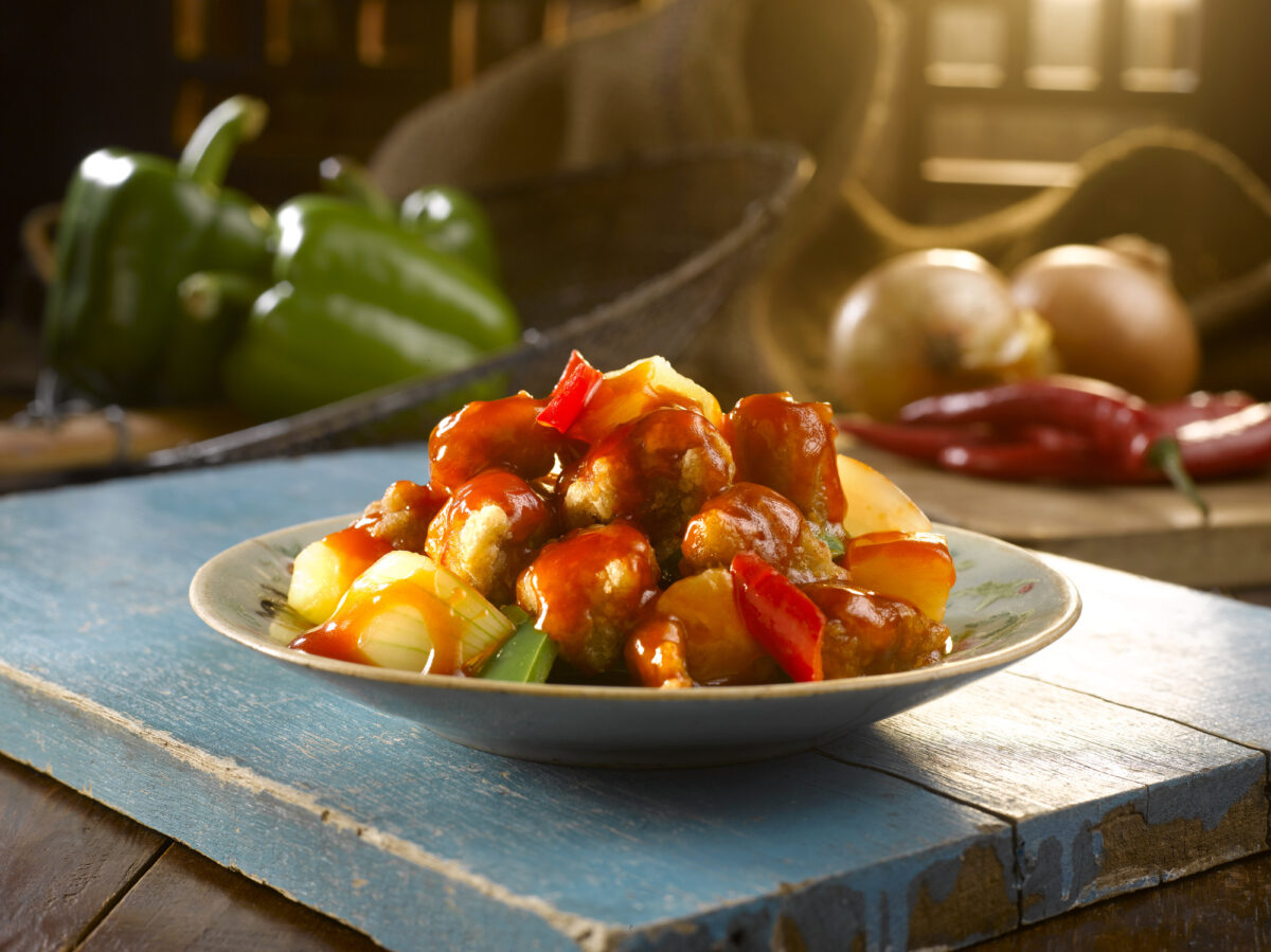 sweet and sour pork served in a dish on blue table with vegetables in background