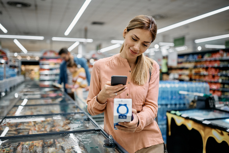 Smiling woman scanning QR code on a product while buying in supermarket.