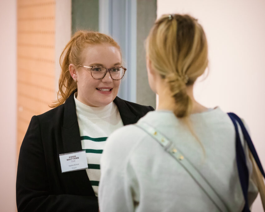 young woman with badge speaking to blonde student