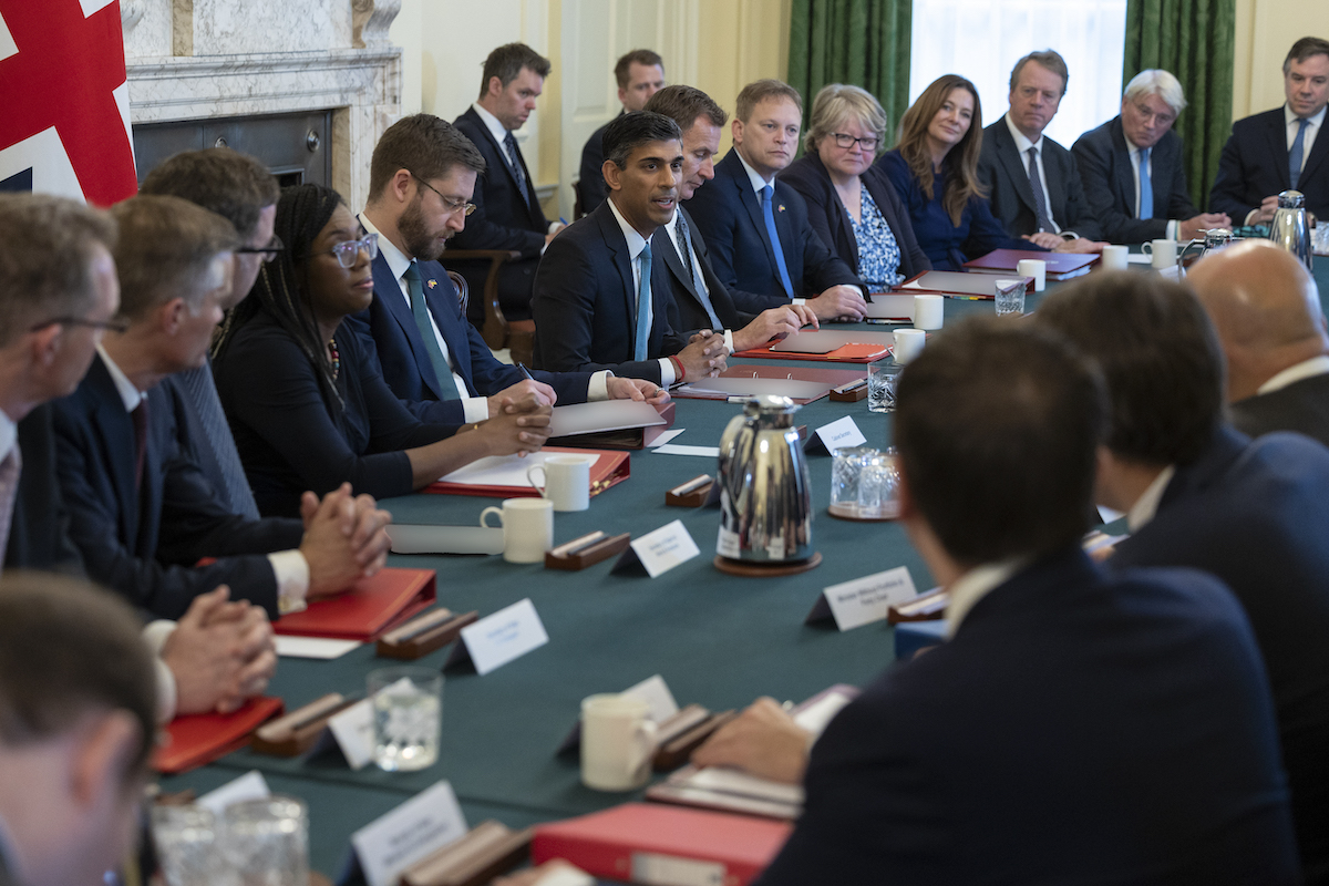 UK Prime Minister talking with colleagues in cabinet meeting, all sat on long green table