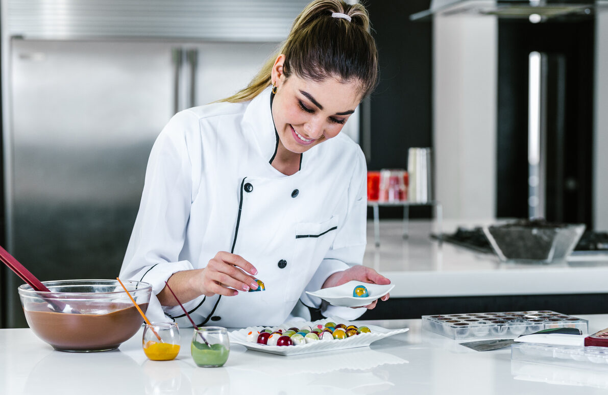young woman chocolatier in chef hat with chocolates on plate in a commercial kitchen