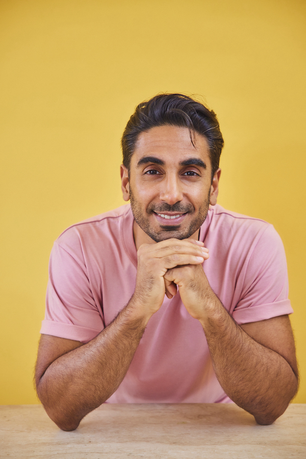 Dr Rupy Aujla in pink t-shirt smiling in front of yellow background