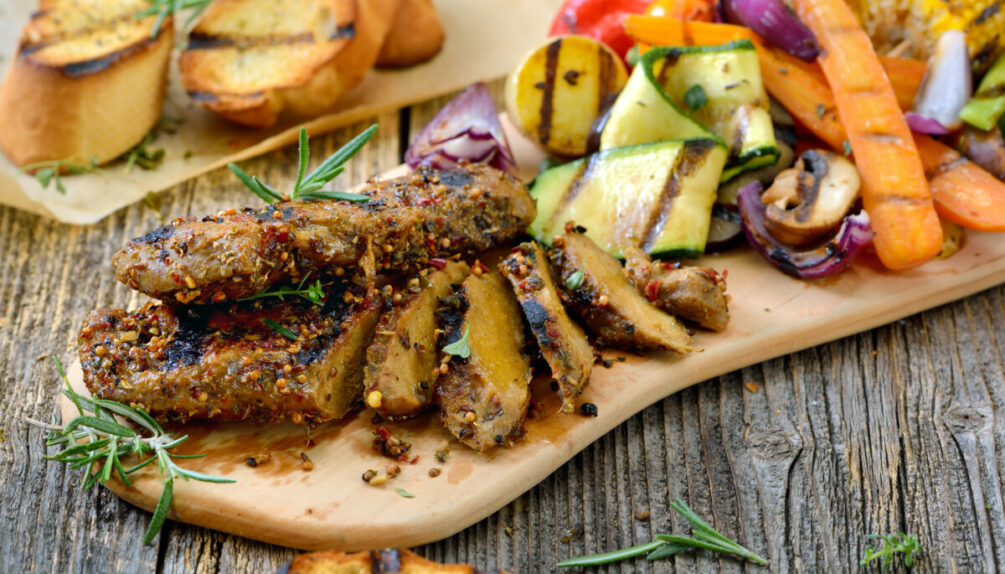 Grilled vegan seitan steaks with mixed vegetables and crusty baguette