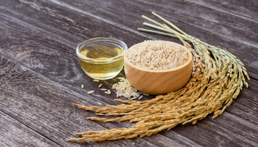 rice bran oil on wooden table with bowl of rice and wheat crop