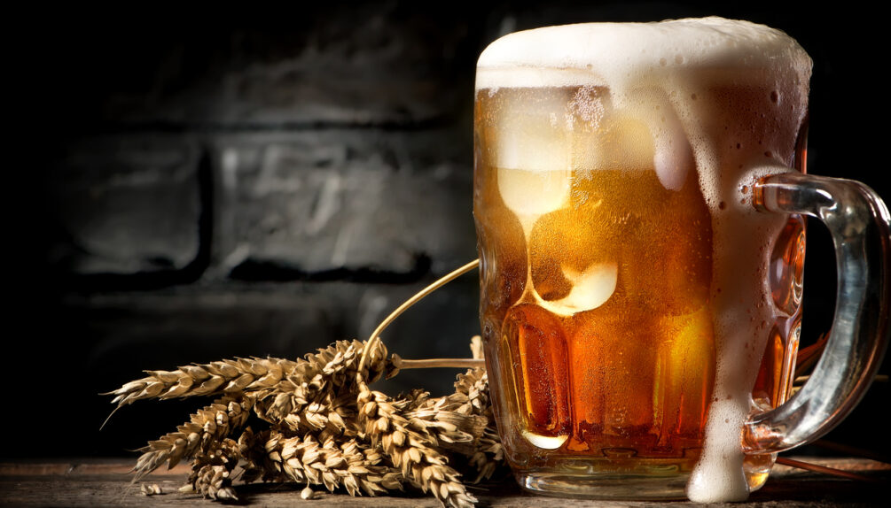 overflowing beer placed alongside some hops