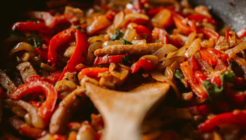 vegan protein pieces with red peppers in pan with wooden spoon
