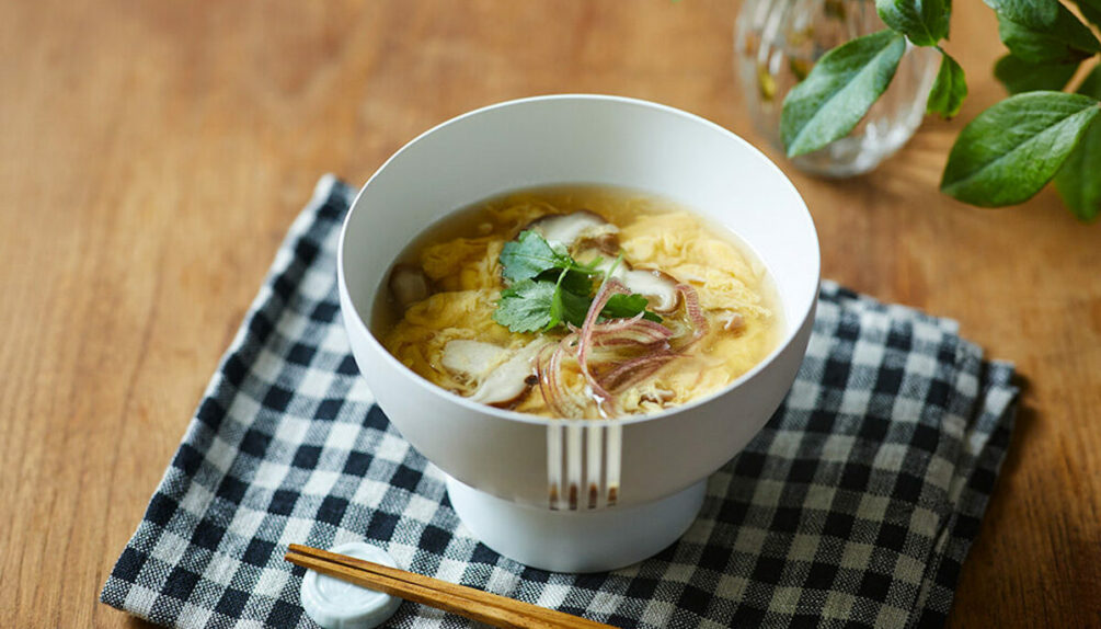 bowl of soup noodles with herbs on a checkered cloth with chopsticks