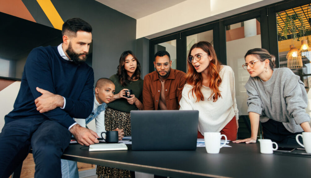 Group of businesspeople having a discussion in a boardroom, looking at a laptop.