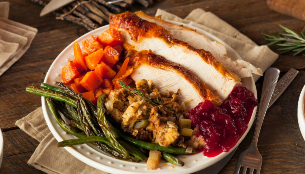 Plate with turkey slices, stuffing and vegetables on wooden table with cutlery and napkins