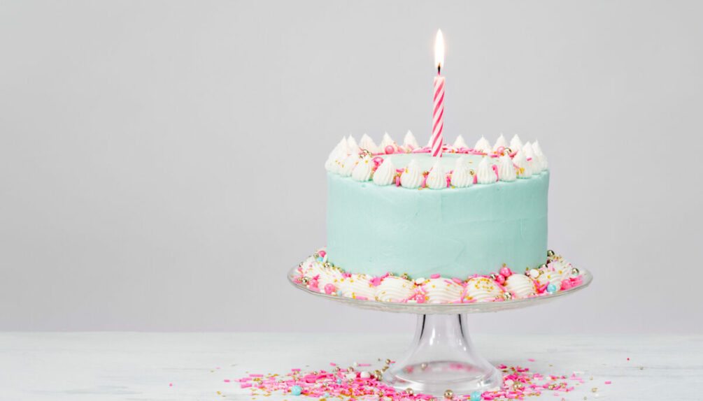 Pastel blue birthday cake over white background with pink sprinkles