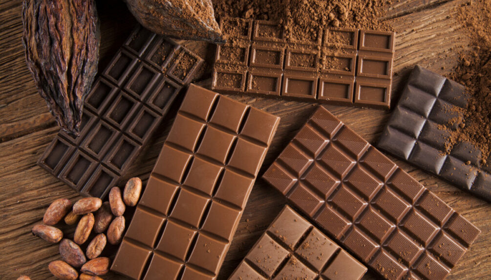collection of chocolate bars on a wooden table alongside cocoa beans