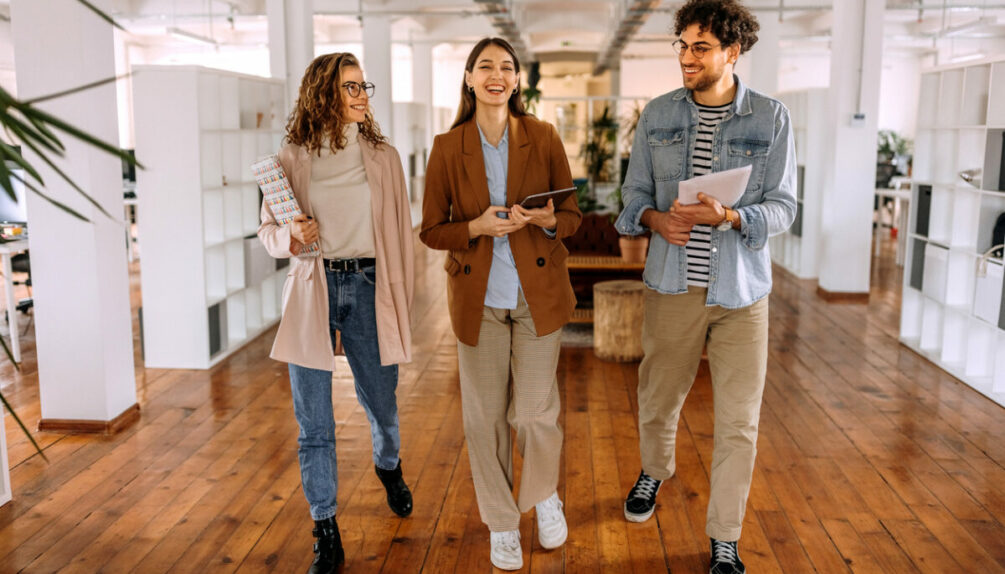 Group of smiling young colleagues walking and talking in modern office