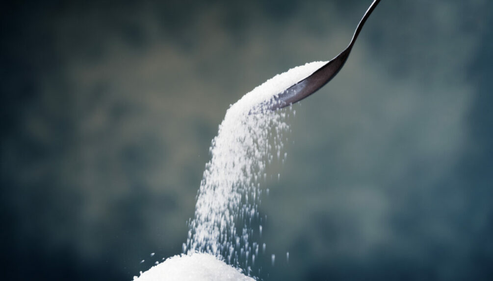 sugar poured from a spoon into small pile, on grey background