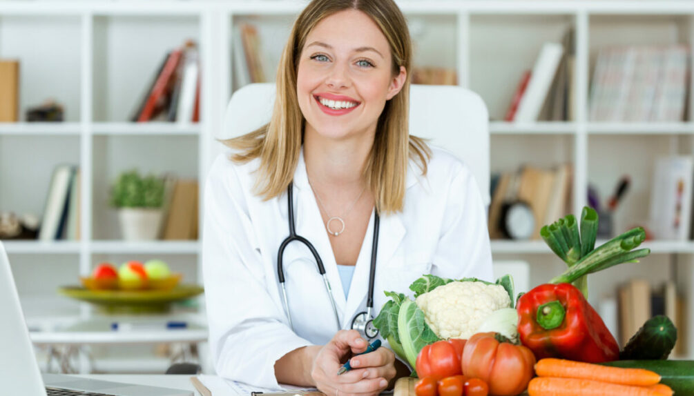 Portrait of beautiful smiling nutritionist looking at camera and showing healthy vegetables in the consultation