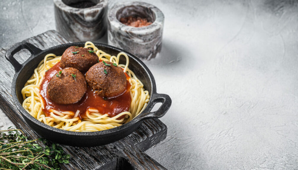 Vegan tomato pasta with plant based Meatballs in a skillet. White background.