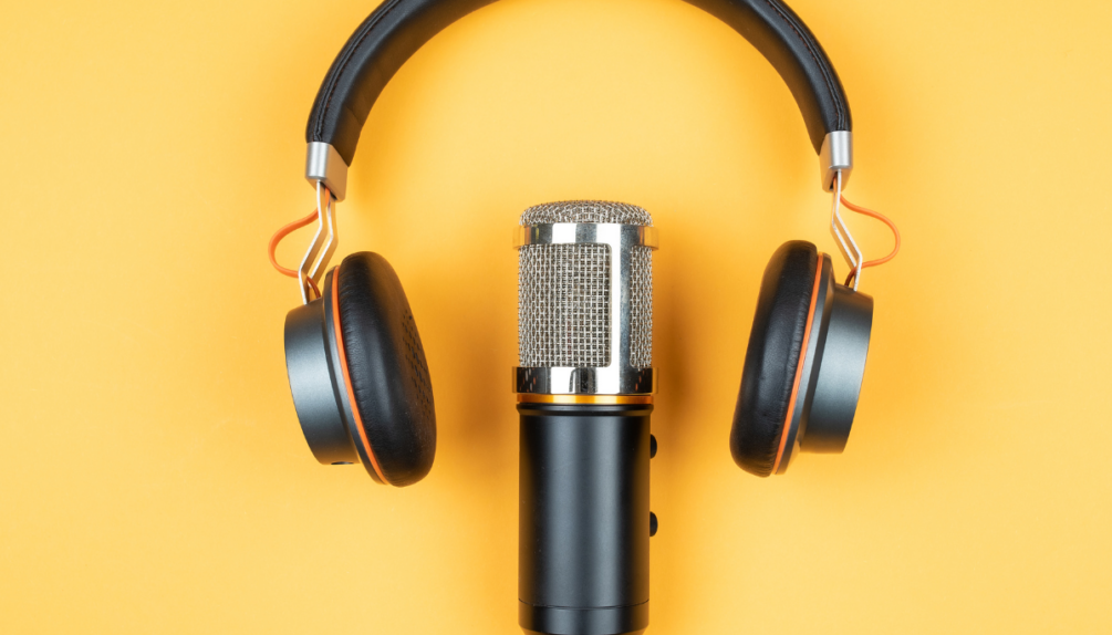A pair of headphones over a microphone against a yellow background, representing podcasting