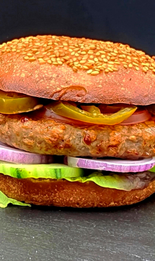An alternative protein burger, complete with bun, jalepenos, patty, red onion and lettuce. On a black table with a black background