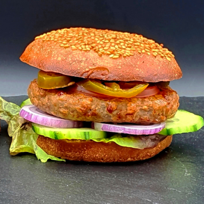 An alternative protein burger, complete with bun, jalepenos, patty, red onion and lettuce. On a black table with a black background
