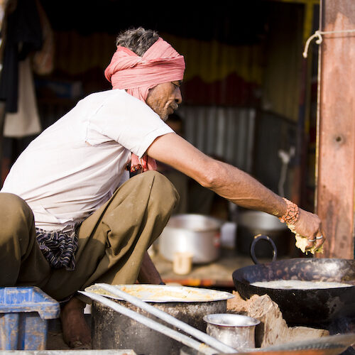 A man cooks over hot oil in Pushkar, India. He is cooking outdoors in red head scarf and white t-shirt