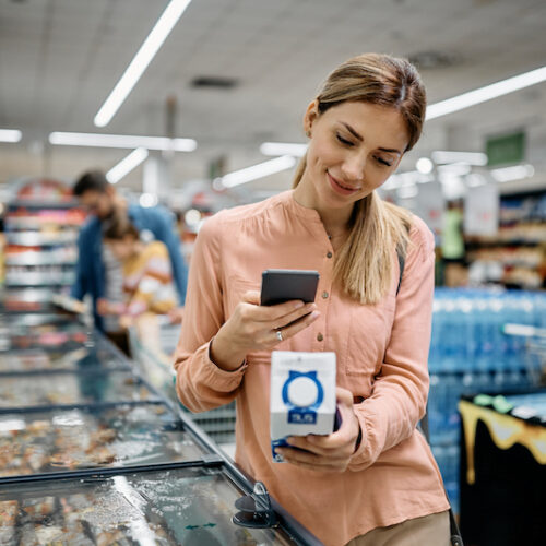 Smiling woman scanning QR code on a product while buying in supermarket.