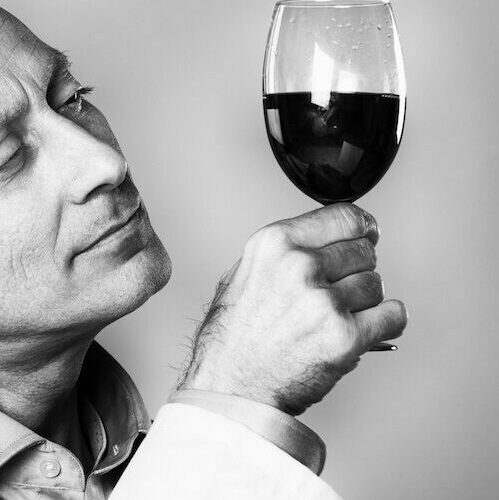 Man in lab coat holds wine glass up to light
