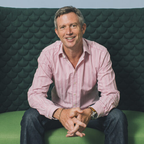 Paul Lindley in shirt and jeans sitting on a green sofa