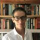 woman with short hair and glasses in front of a bookshelf